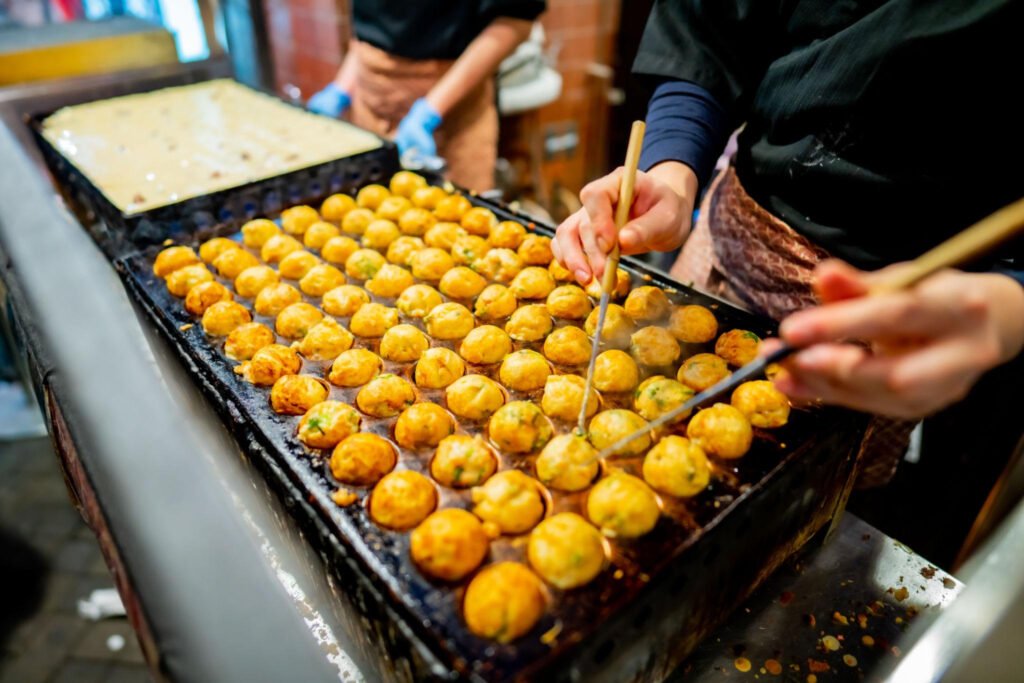 Fresh takoyaki being cooked on a traditional round griddle in Osaka, Japan